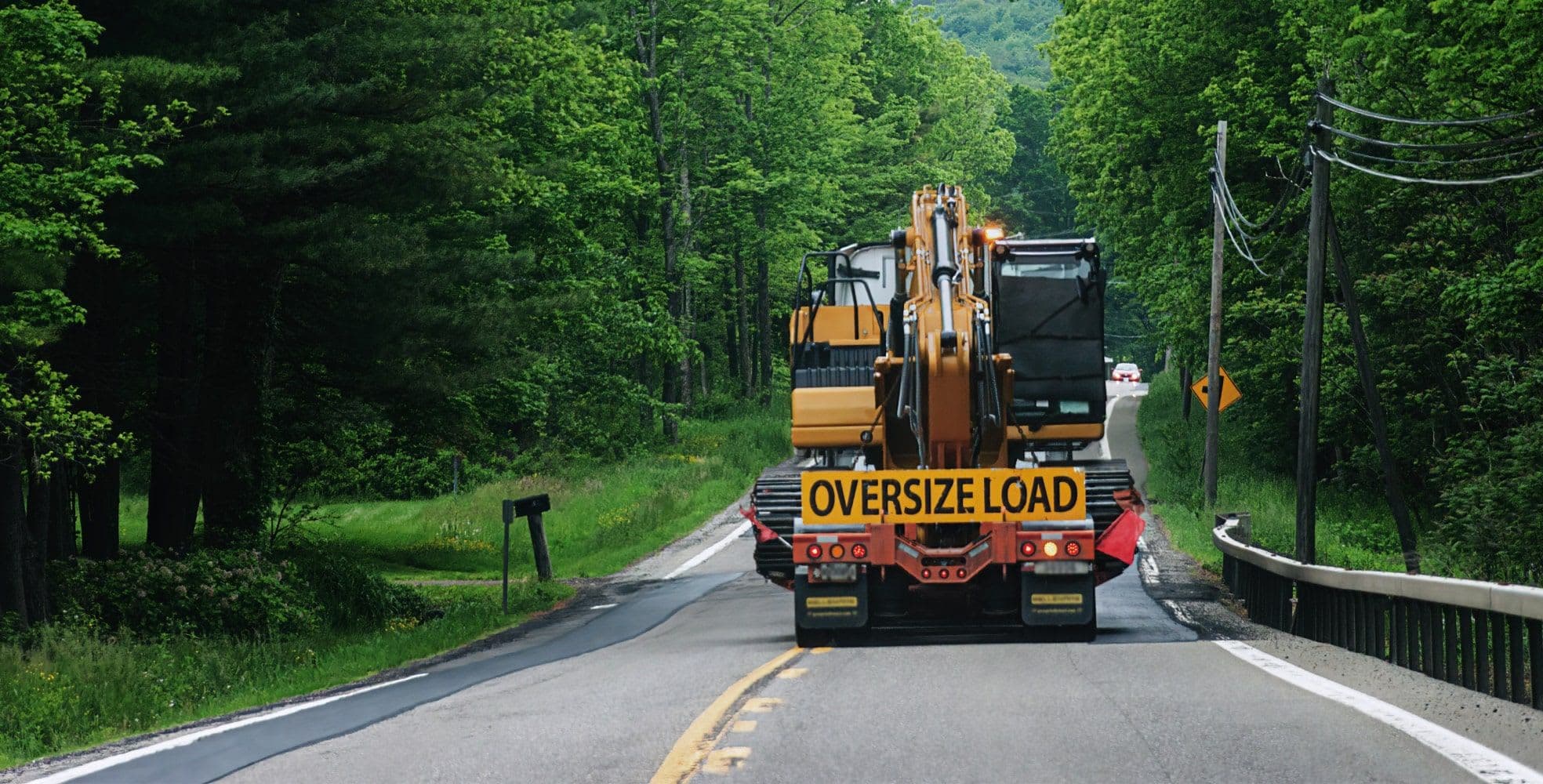 Construction equipment being hauled down a road by a truck reading "oversize load"