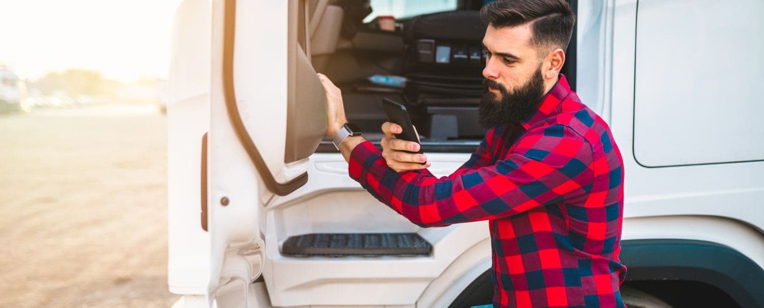 Freight driver standing by his truck using the Wize Drive app from Wize Load to find his next haul.
