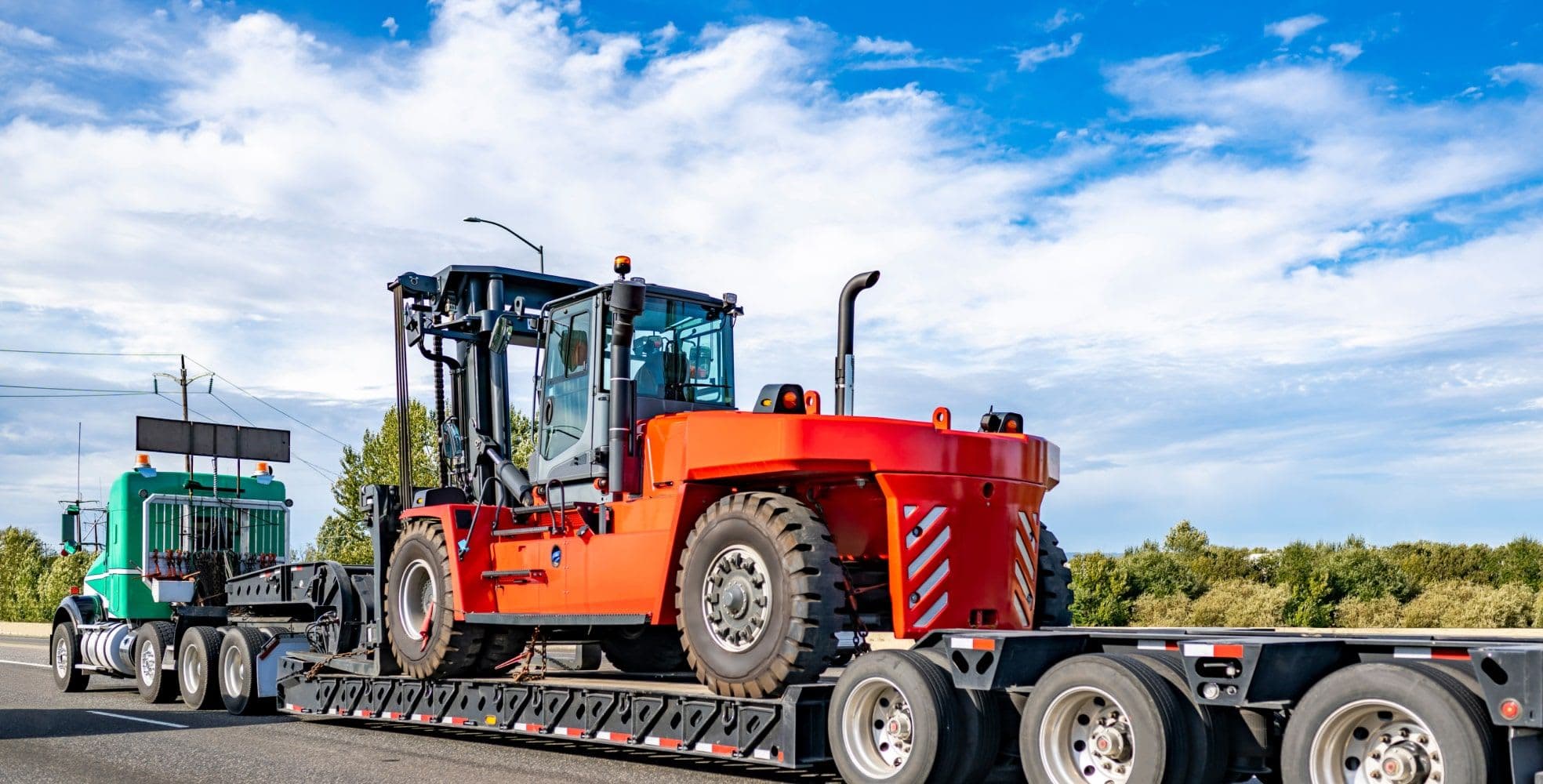 flat bed Truck carrying a large orange tractor down a street
