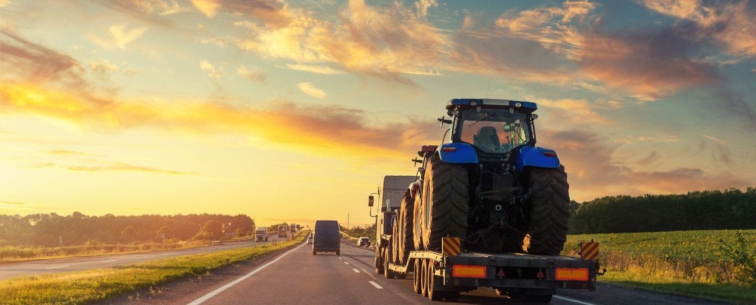 A truck hauling a tractor to a nearby farm at sunset